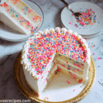 Close-up of two slices of Funfetti cake topped with vanilla frosting and colorful sprinkles on a white plate with gold rim.